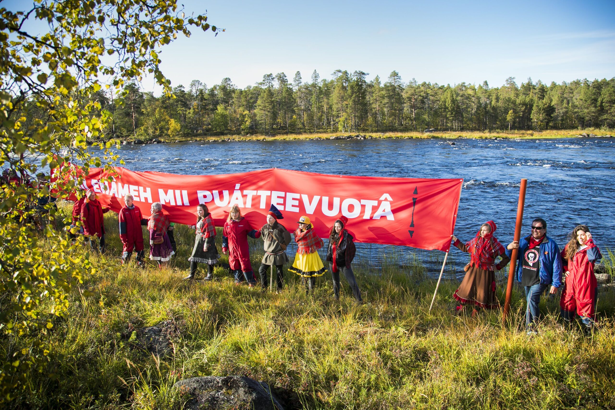 Rataa vastustettiin myös Jäniskoskella. Tällä kertaa banderollin teksti oli kirjoitettu inarinsaameksi. Kuvassa keskellä Jenni Laiti vierellään muusikko ja runoilija Niilas Holmberg.