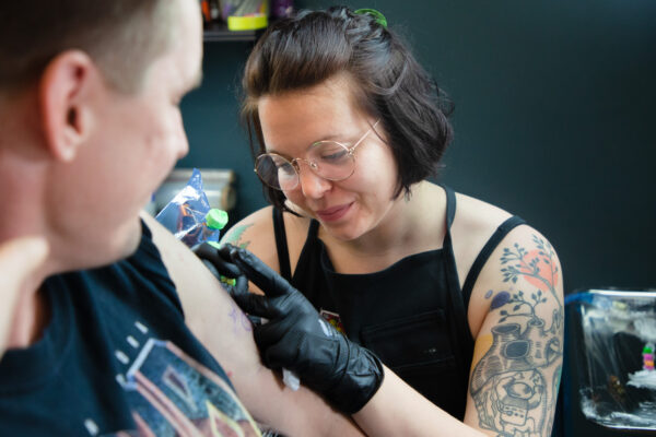 Nazarenko hymyilee ja tekee tatuointia asiakkaan olkavarteen.