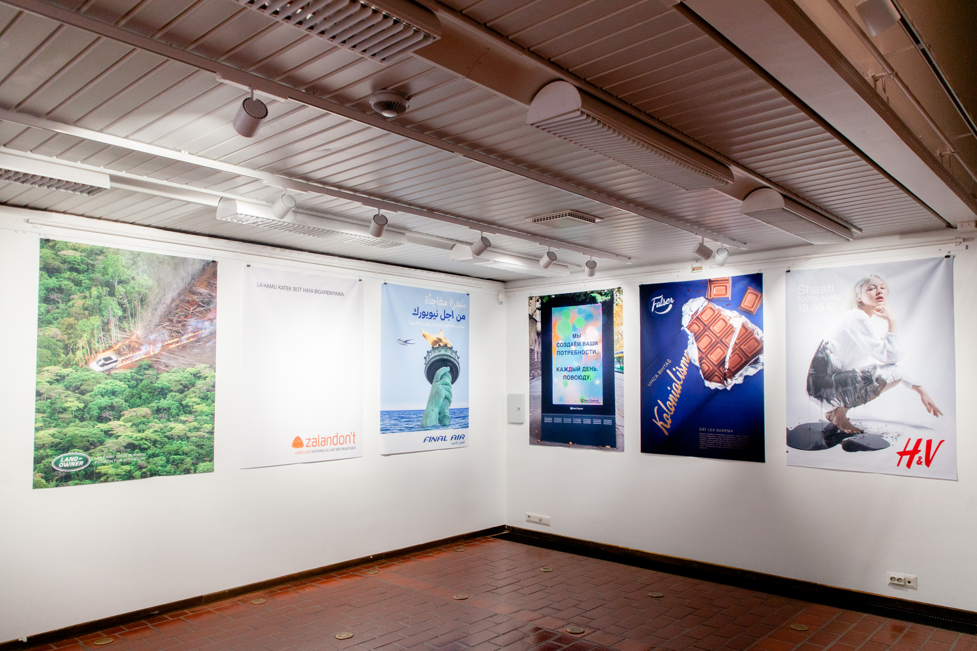 Näyttelytila, seinälle ripustettu kuusi vastamainosta.