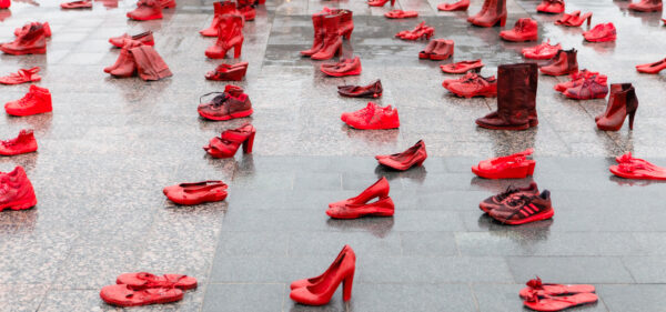Monia punaiseksi maalattuja kenkiä aseteltuna sateen kastelemalle asfaltille.