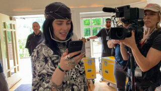 Billie Eilish katsoo kännykkäänsä kuvausryhmän kuvatessa häntä