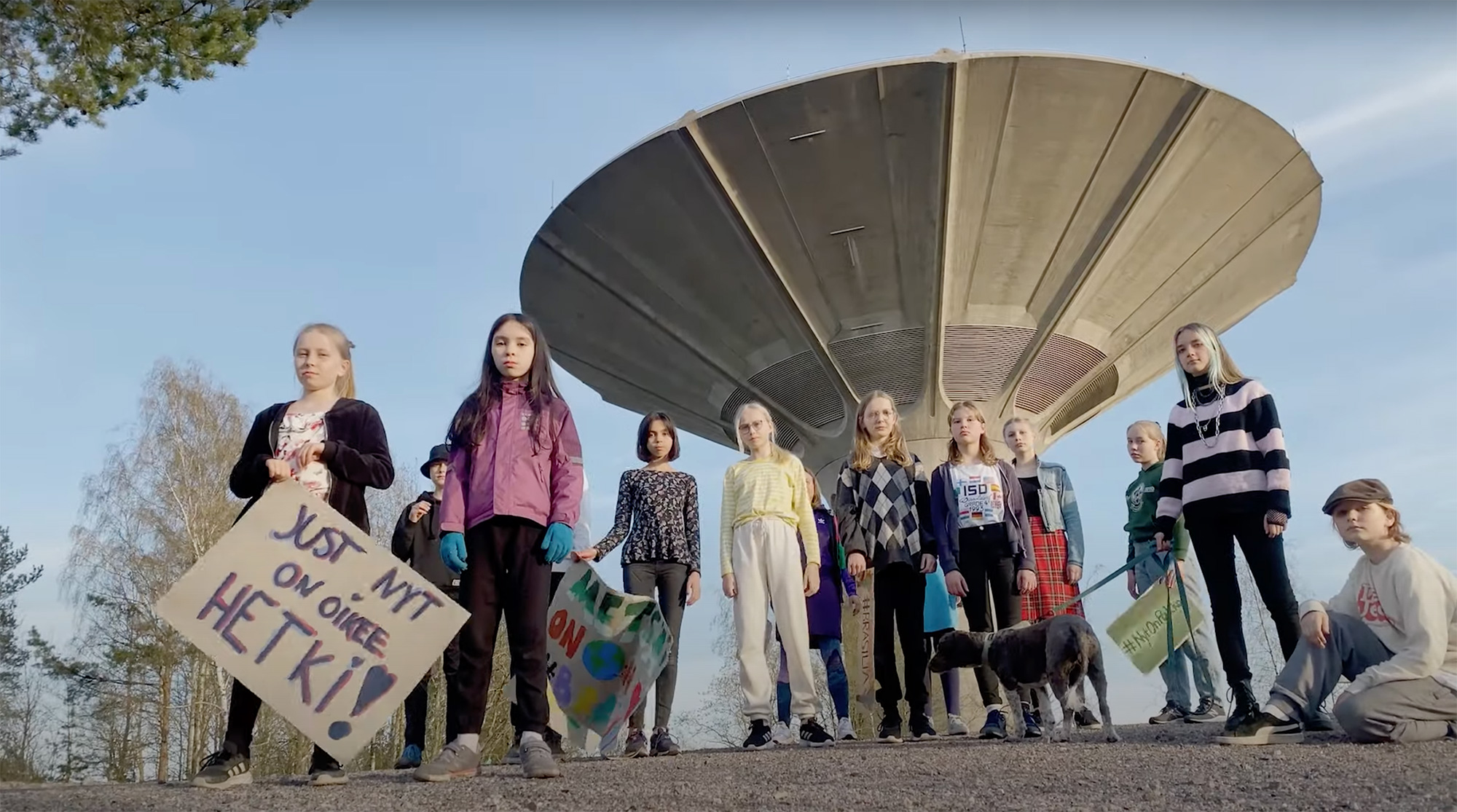 Lapset seisovat vesitornin edessä kyltit käsissään. Kylteissä lukee esim