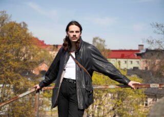 Vaarakallio nojaa kaiteeseen, taustalla puita ja kerrostaloja.