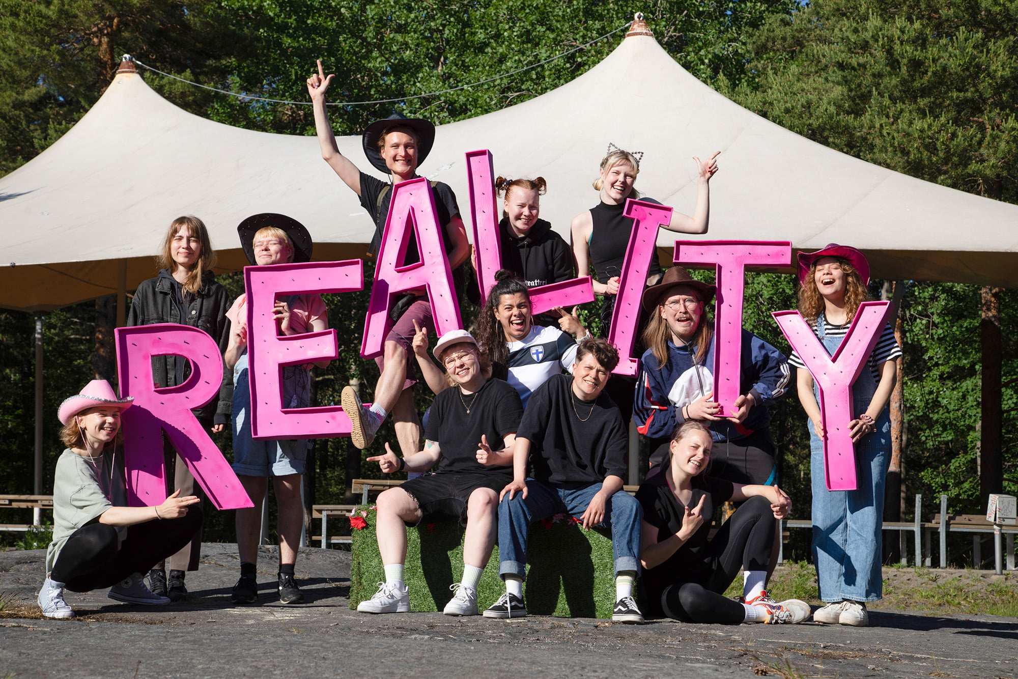 Joukko nauravia ihmisiä, pitelevät käsissään kirjaimia, jotka muodostavat sanan