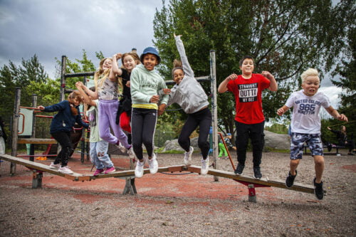 Ryhmä iloisia lapsia hyppää leikkitelineeltä maahan.