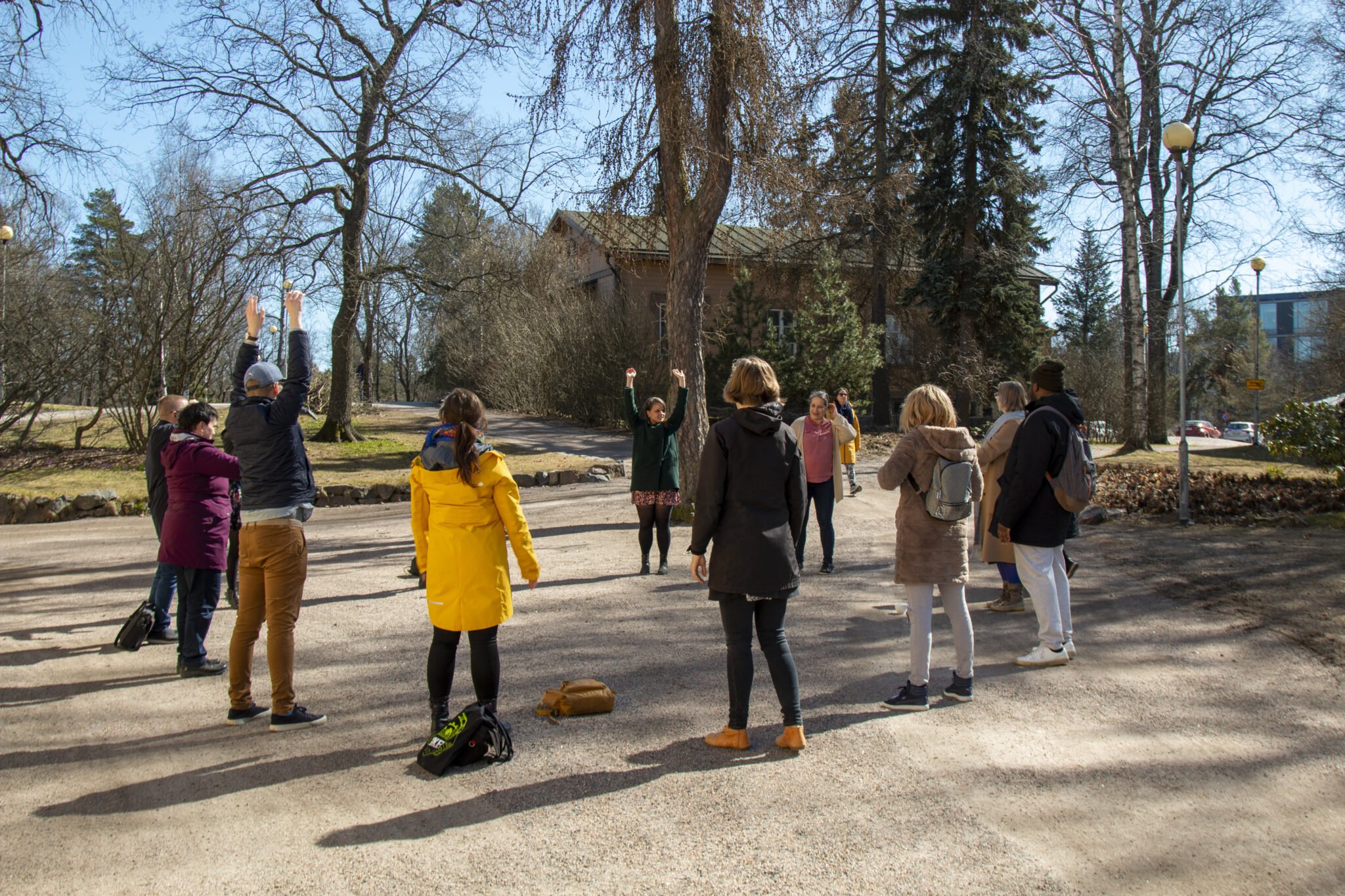 Ryhmä aikuisia seisoo ringissä keväisellä pihamaalla