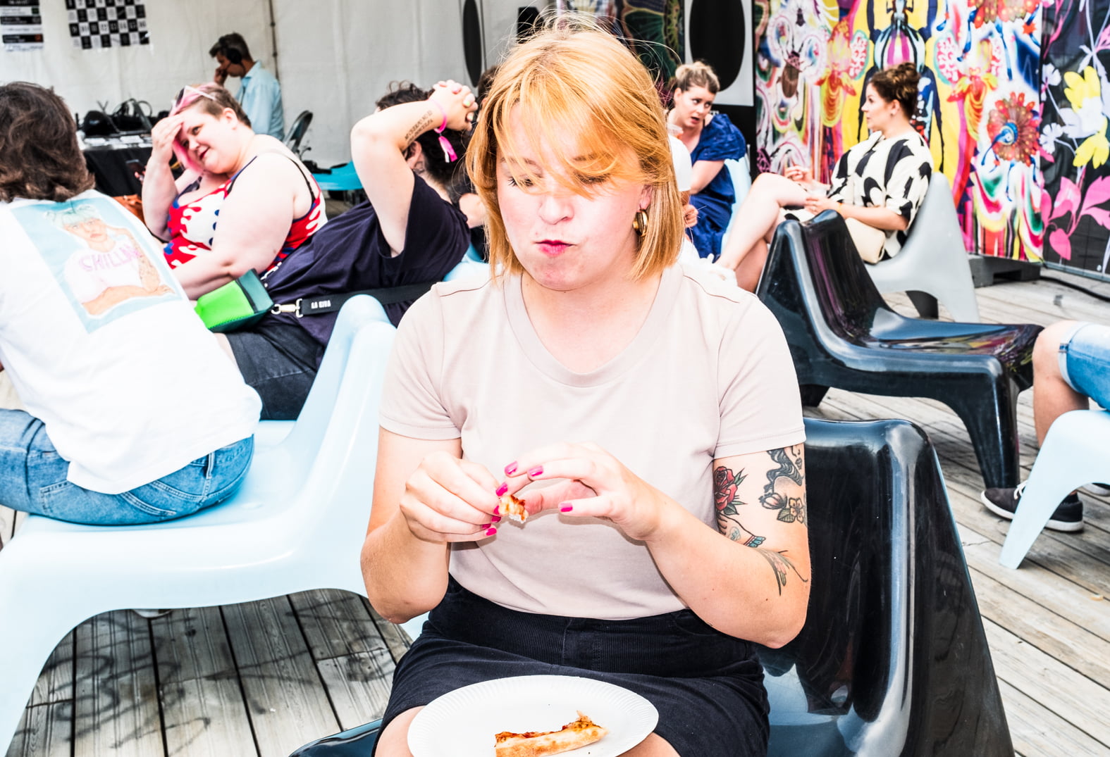 Alma Onali syö pitsaa, takana istuu ihmisiä mukavalta näyttävillä tuoleilla