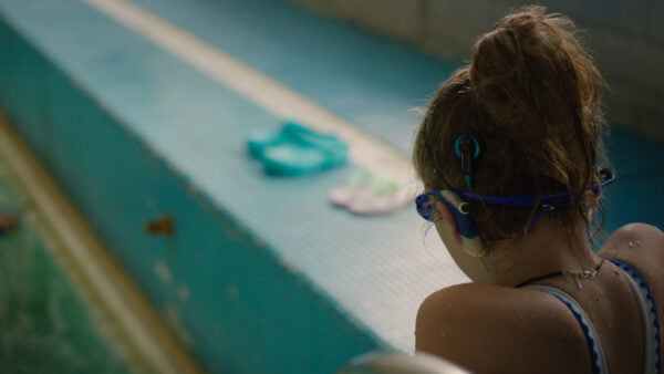 Tyttö istuu uima-altaan reunalla, kuulolaite näkyy korvalla