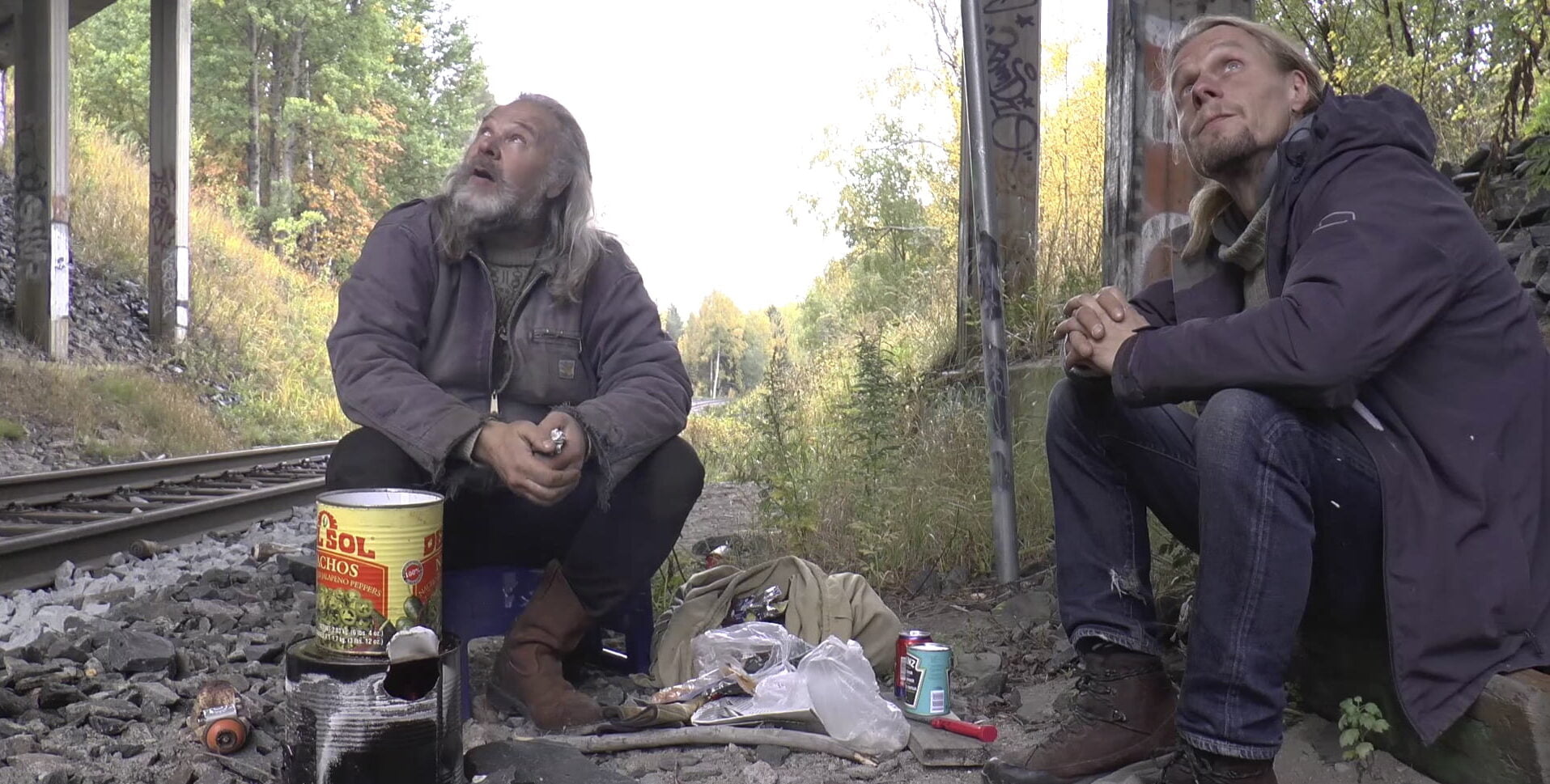 Kaksi henkilöä istuu junaradan varressa.