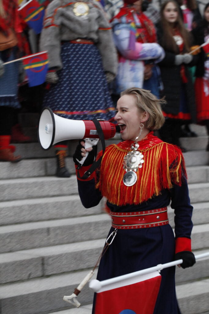 Mielenosoittajia Eduskuntatalon portailla. Petra Laiti huutaa megafoniin.
