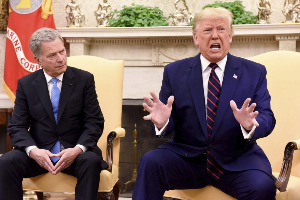Presidentit Sauli Niinistö ja Donald Trump istuvat rinnakkain. Trump huutaa ja heiluttaa käsiä, Niinistö katsoo häntä vakavasti.