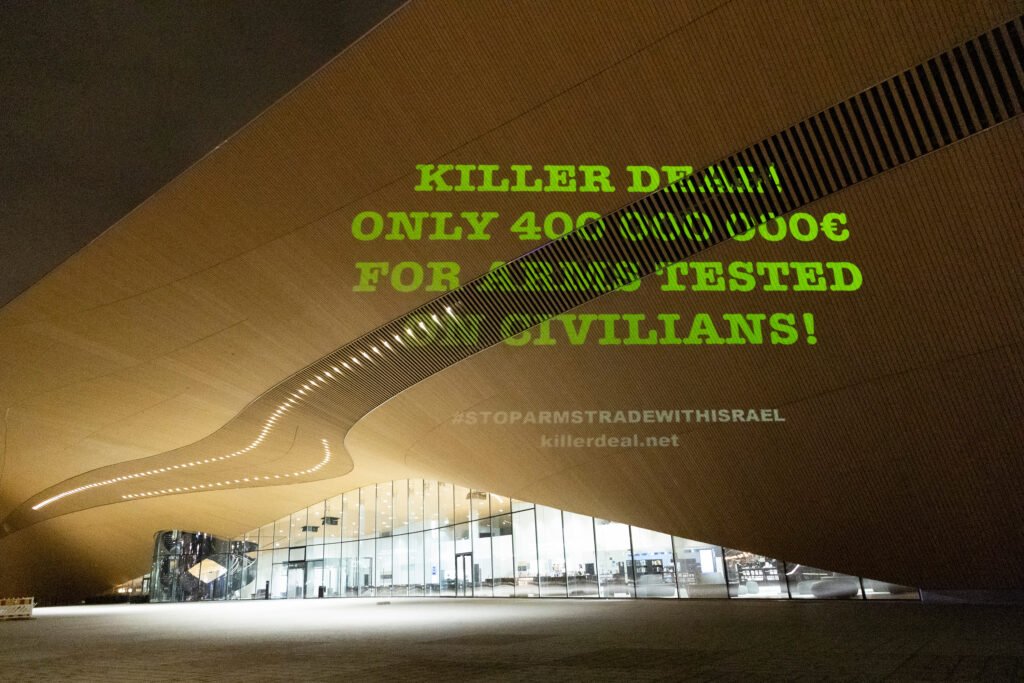 Teksti “Killer Deal! Only 400 000 000 € for Arms Tested on Civilians!” heijastettu Helsingin keskustakirjasto Oodin seinään.