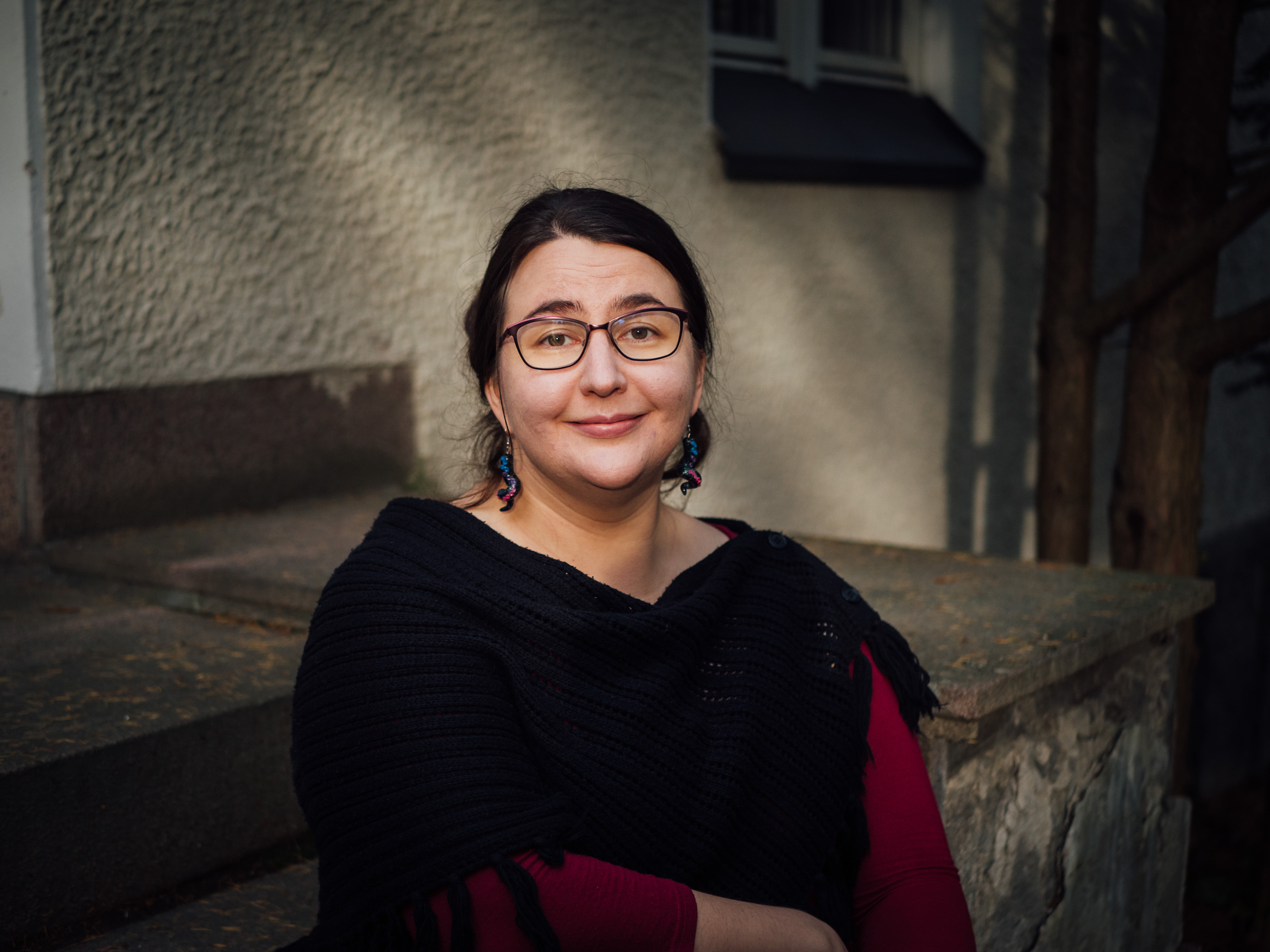 Reetta Vuokko-Syrjänen katsoo kameraan hymyillen, taustalla harmaata seinää.