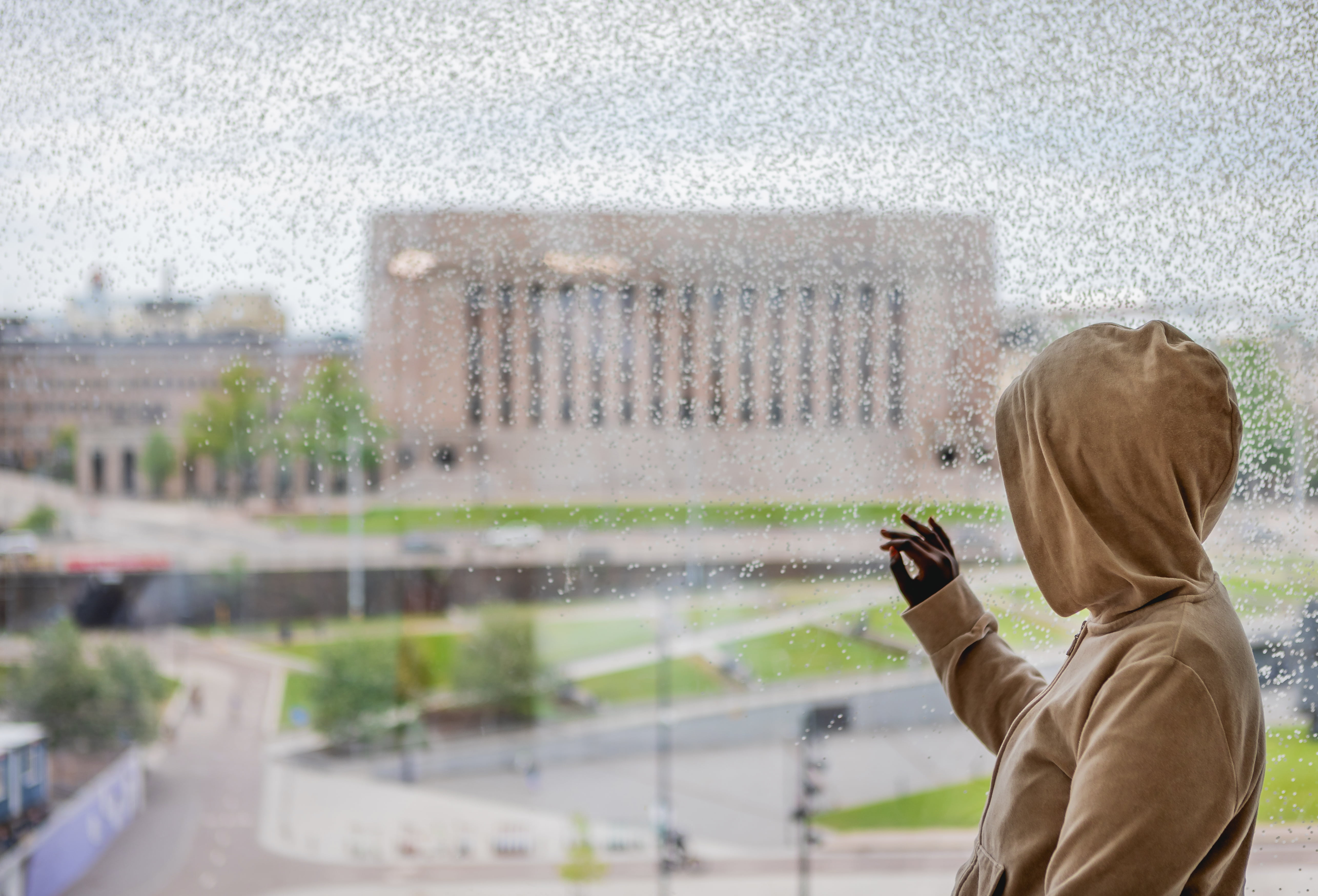 Ihminen katsoo ikkunan läpi eduskuntataloa.