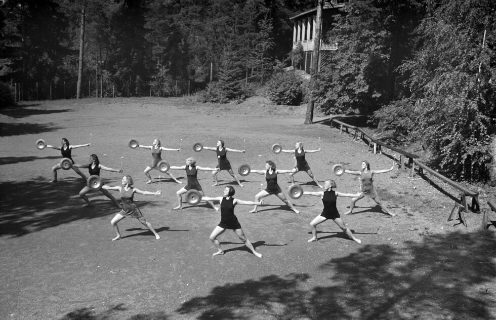 Mustavalkoisessa kuvassa joukko naisia voimistelee ulkoilmassa.