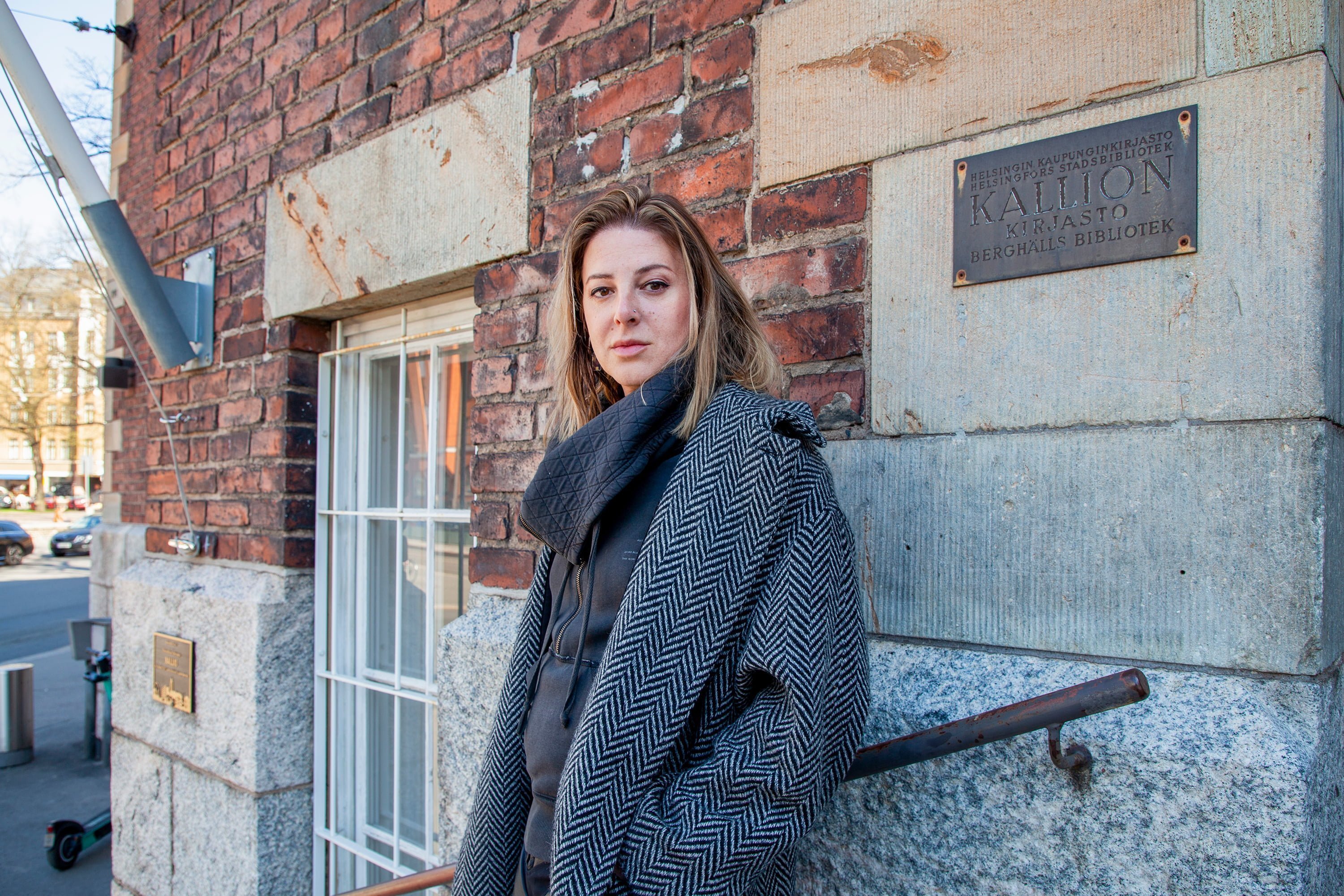 Torrey Peters nojaa Kallion kirjaston seinään, katsoo kameraan.