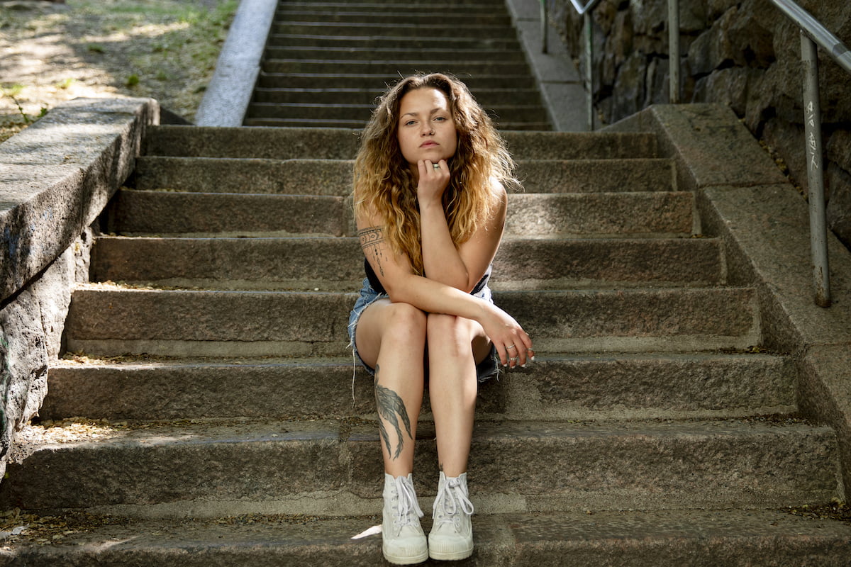 Raakasaga istuu kivisillä portailla kohden kameraa. Nojaa kämmenellä leukaan.