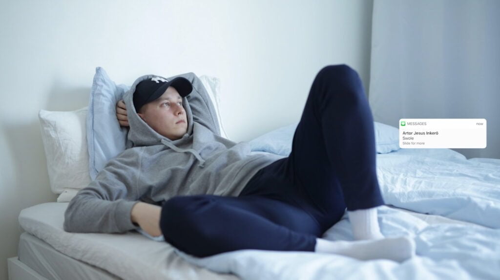 Sinisen sävyinen valokuva, henkilö makaa sängyssä. Kuvan päällä näyttökaappaus tekstiviestistä, jossa lukee "Swole".