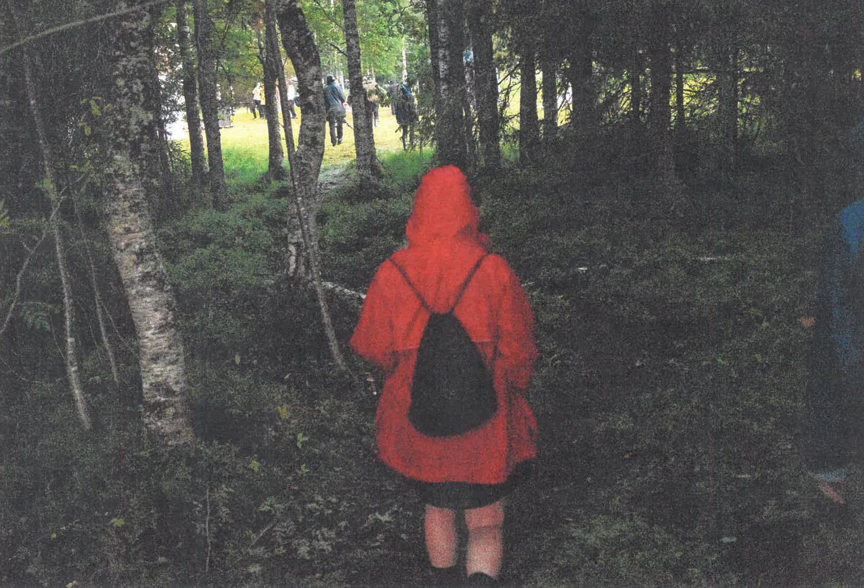 Punatakkinen henkilö kulkee metsän läpi.