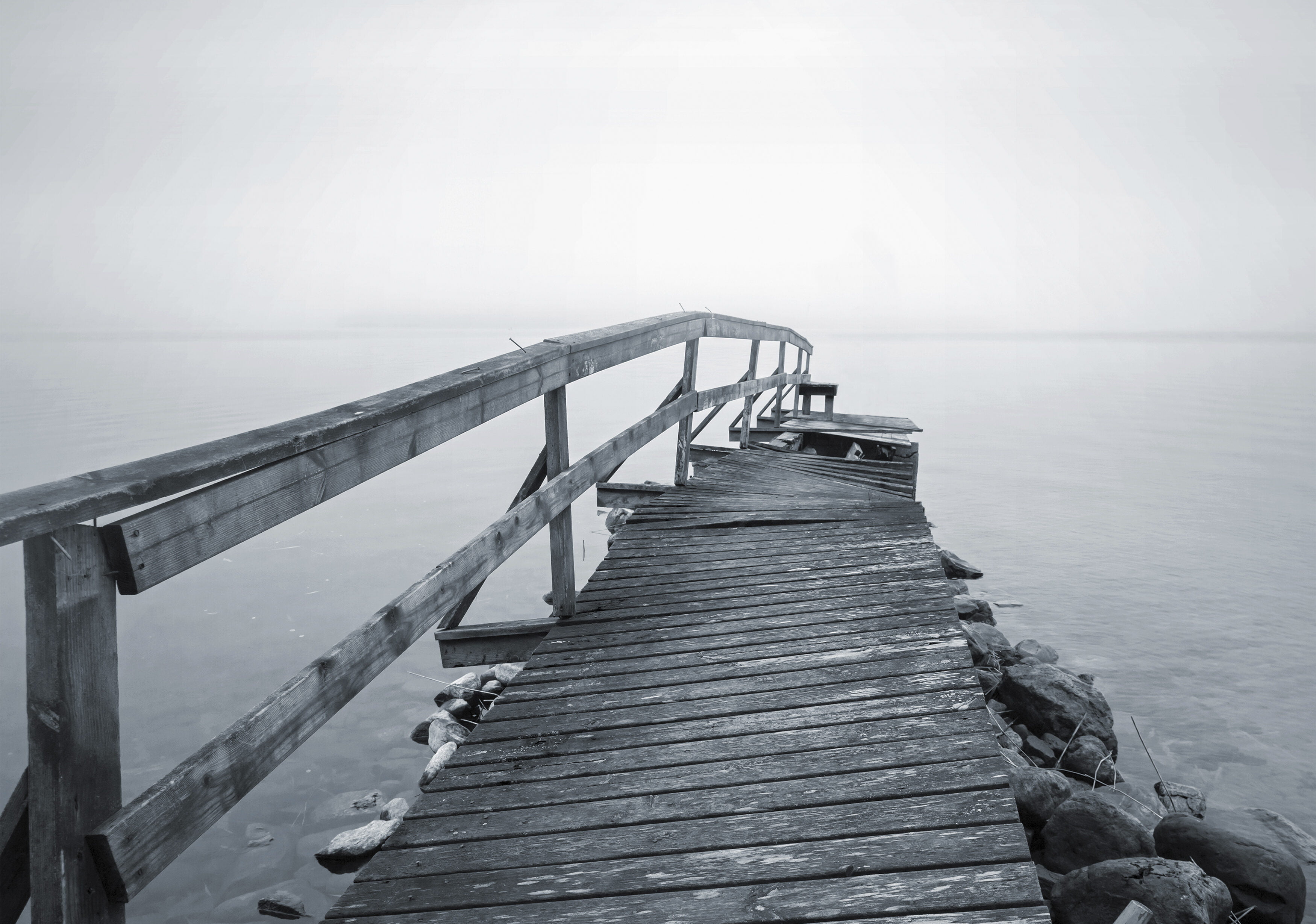 Mustavalkoinen kuva, rikkinäinen laituri meren rannassa.
