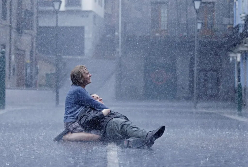 Kaksi ihmistä maassa, kovassa sateessa.