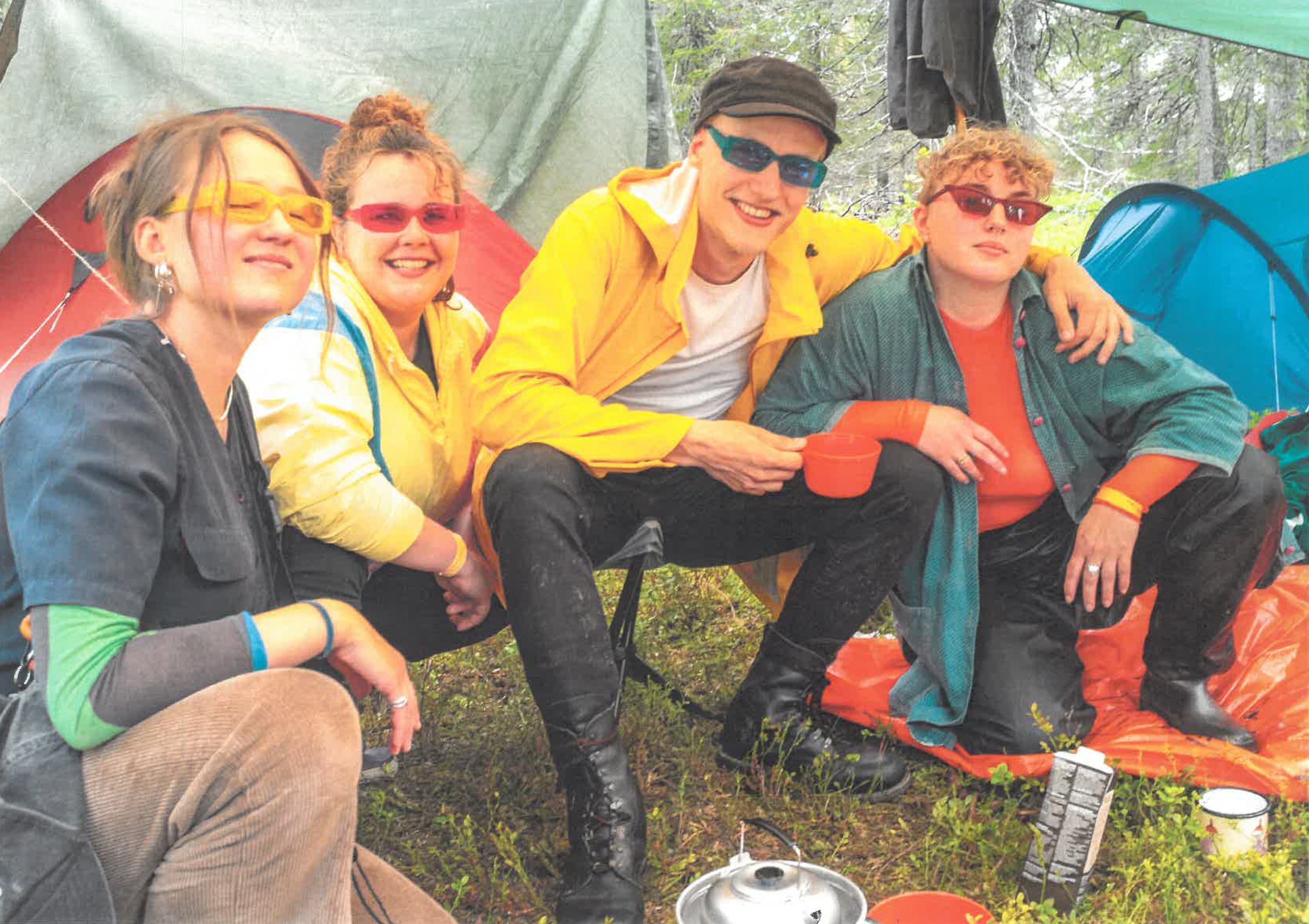Neljä henkilöä värikkäissä aurinkolaseissa poseeraavat kameralle telttojen edessä.