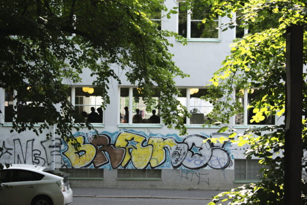 Valokuvassa koulu, ikkunasta näkyy ihmisten hahmoja, seinässä graffiti.