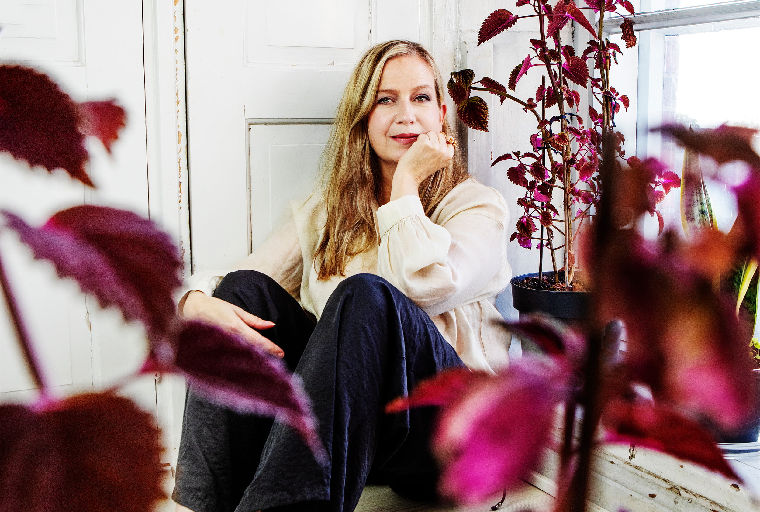 Salmenkallio istuu ikkunalaudalla, katsoo kameraan hymyillen.