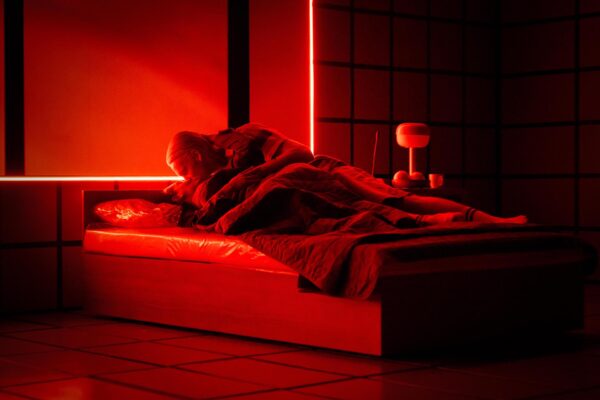 Punaiseksi valaistu huone. Kaksi näyttelijää suutelee toisiaan sängyllä.