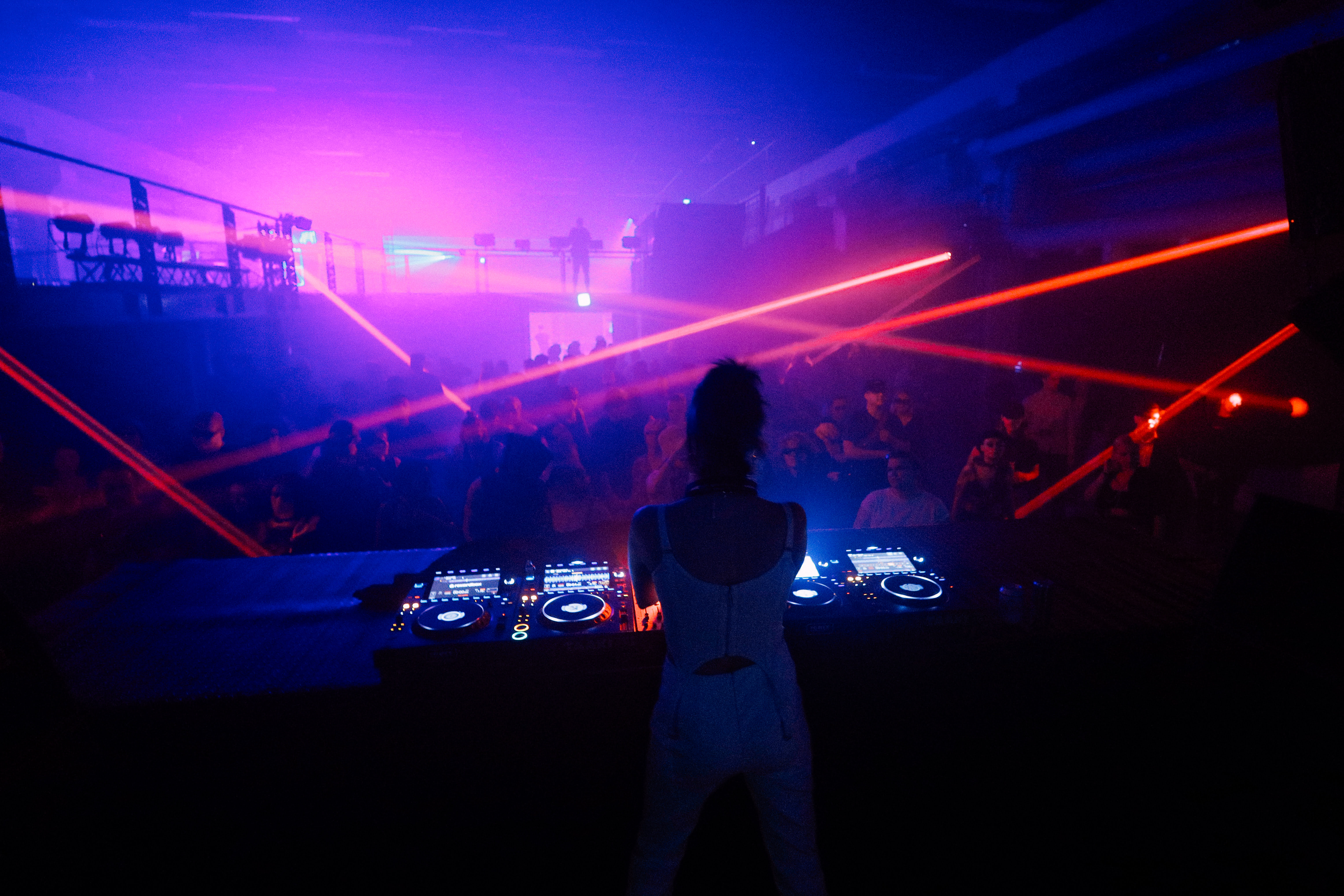 Laaja kuva hämärästä klubista, kuvattu yleisöä dj-pöydän takaa.