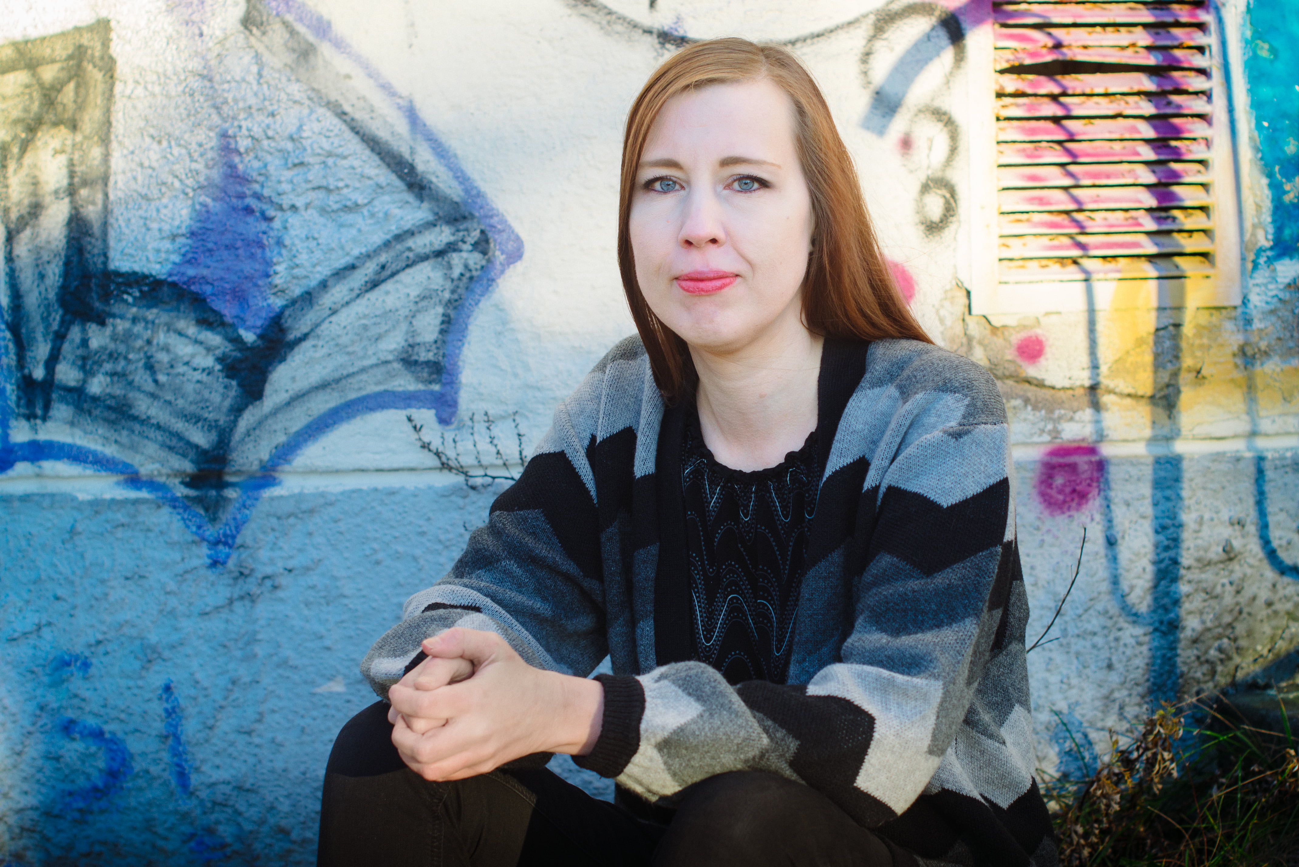 Eeva-Maria Grekula katsoo kameraan, taustalla graffitia.