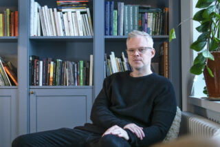 Olli Pyyhtinen kuvattuna työhuoneessa. Taustalla kirjahylly.