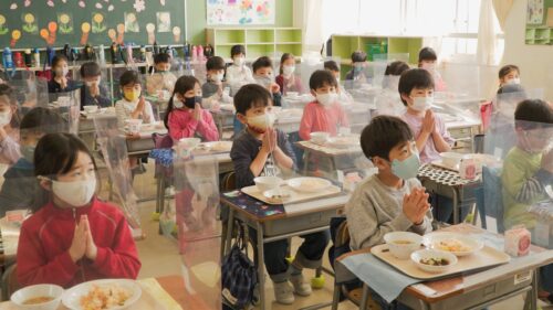 Kuva elokuvasta Kouluvuosi japanissa. Oppilaat ruokailemassa maskit kasvoilla luokkahuoneessa.