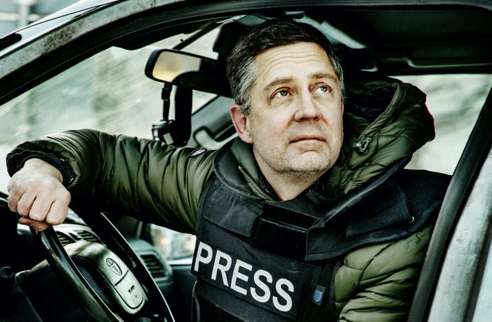 Antti Kuronen istuu auton ratissa luotiliivit päällä, joissa lukee "press"