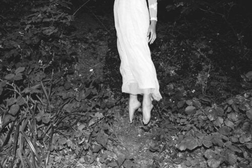 Mustavalkoinen kuva, jossa valkoiseen mekkoon pukeutunut henkilö kohoaa aavistuksen maasta