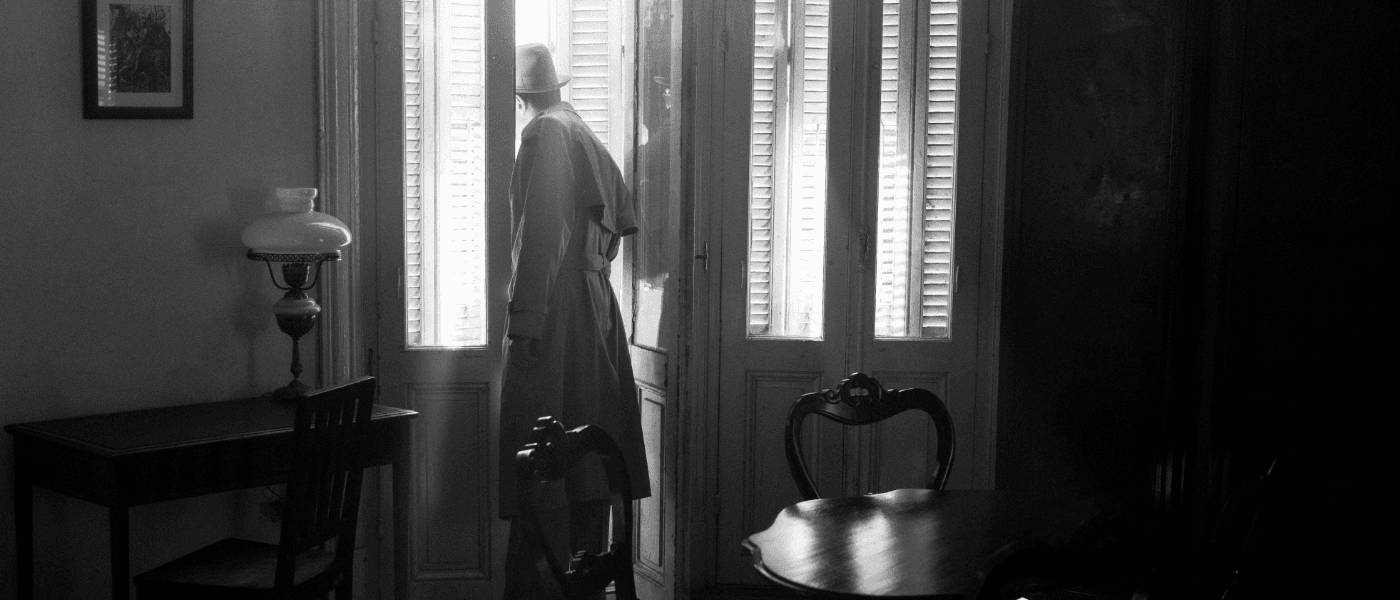 Hattupäinen mies, jolla on pitkä takki, katsoo ulos ovesta