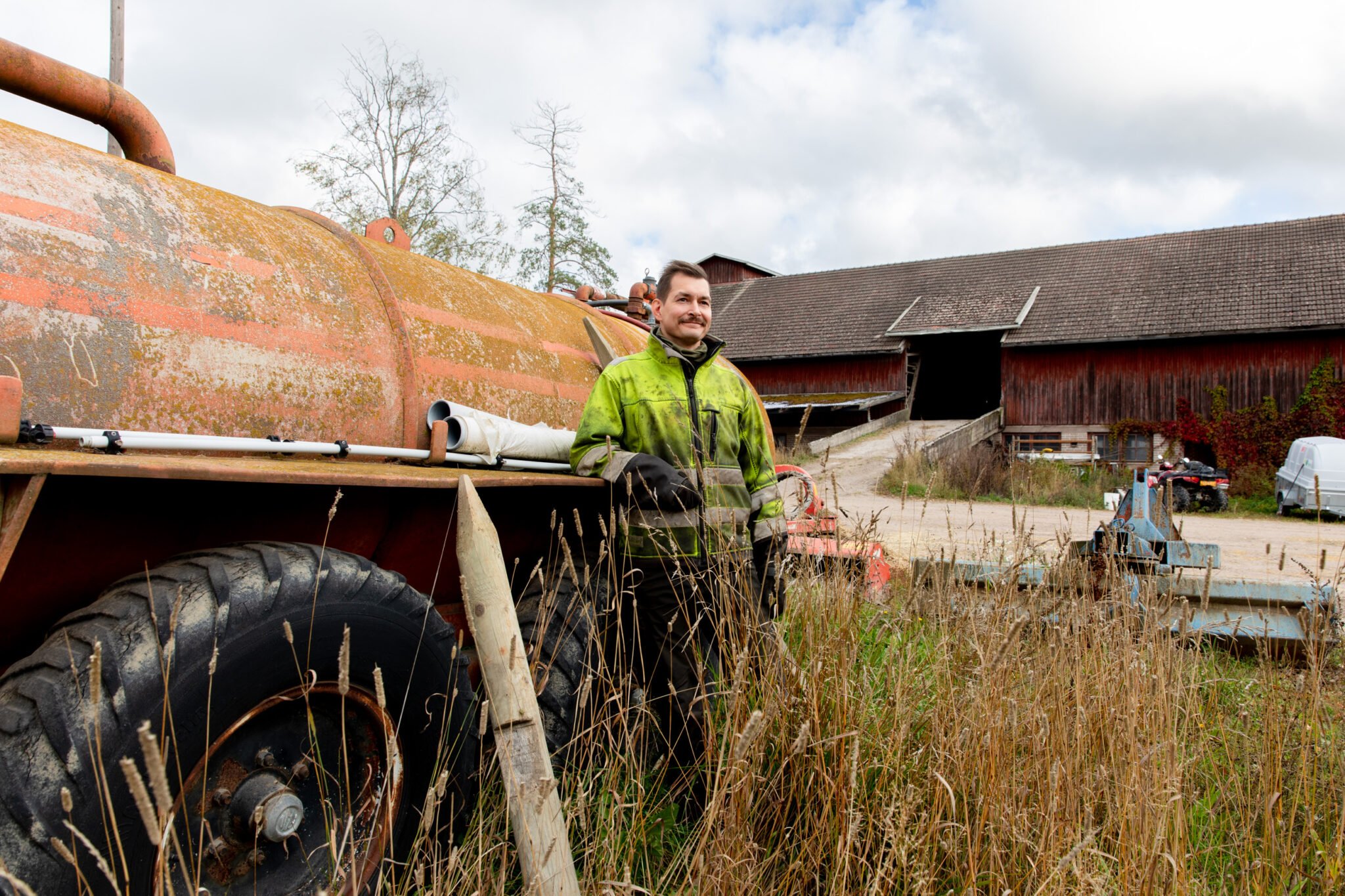 Kyrö nojaa lannoituslaitteeseen, taustalla maatalousrakennus.