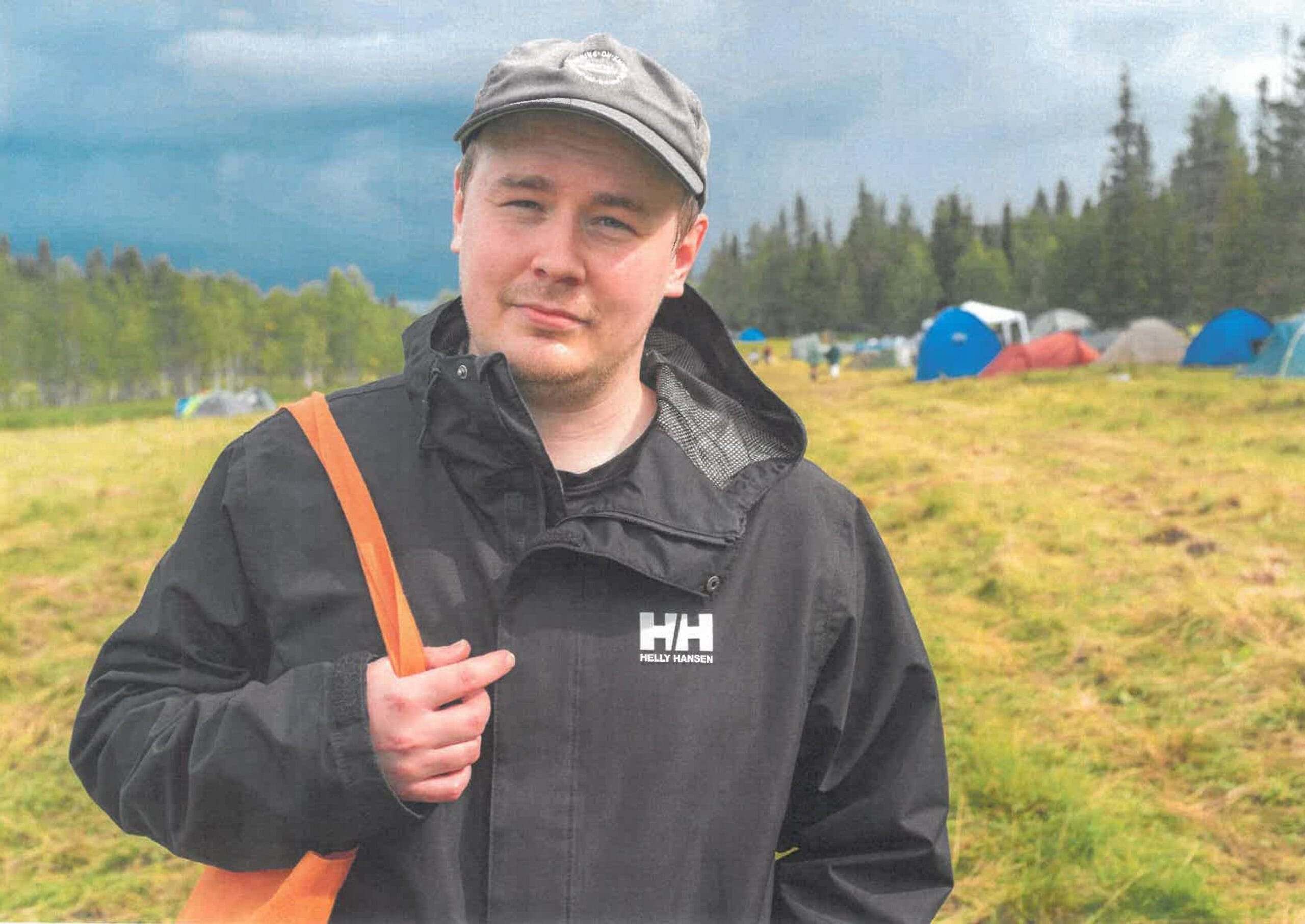 Mies mustassa takissa ja lippalakissa katsoo kameraan. Taustalla golfkentän niittyä.