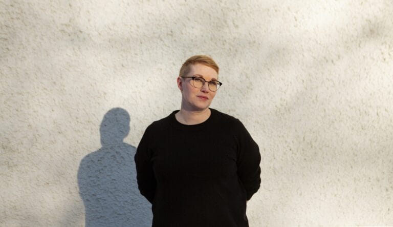 Emilia Miettinen katsoo kameraan hymyillen, taustalla harmaa seinä.