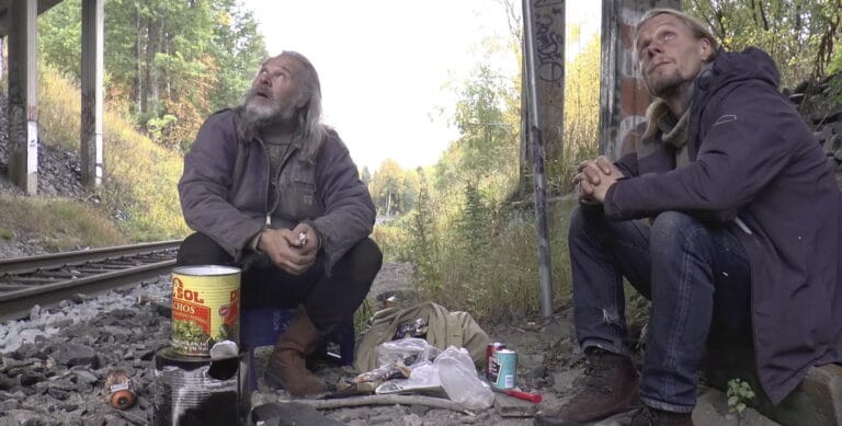 Kaksi henkilöä istuu junaradan varressa.