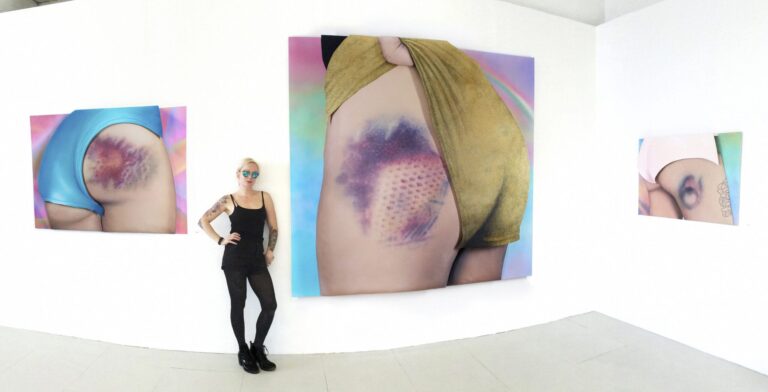 Riikka Hyvönen poseeraa teostensa edessä galleriassa.