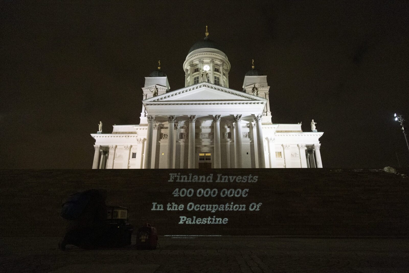 Teksti “Finland Invests 400 000 000 € in the Occupation of Palestine” heijastettu Tuomiokirkon portaille.