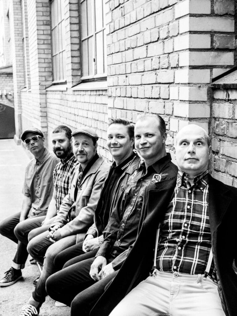Mustavalkoinen kuva Valkyrians-bändistä, jäsenet istuvat penkillä rivissä.